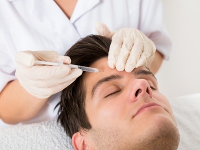 Man lying down with eyes closed while receiving an injection in his forehead