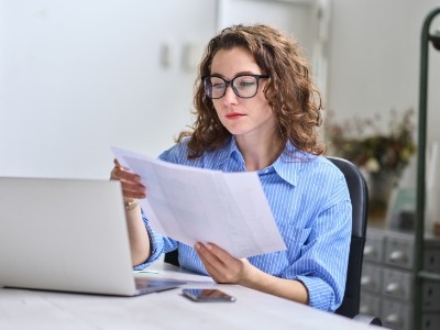 Woman looking at papers while sitting at desk with laptop