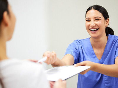 front desk dental staff member handing paperwork to a patient