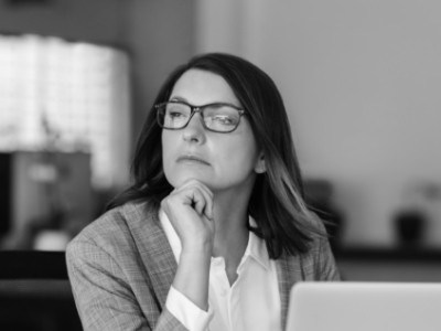 Woman sitting at desk with computer resting her head on her chin and looking pensive