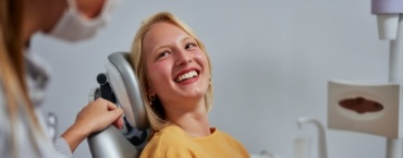 Blonde woman in yellow shirt grinning while sitting in dental chair