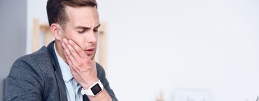 Man in business attire holding the side of his jaw in pain