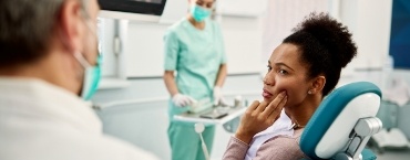 Woman in dental chair pointing to her hurting jaw