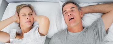 Woman in bed covering her ears while man snores next to her