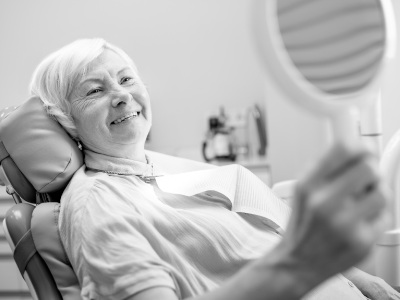 Senior woman checking smile in mirror at dental office