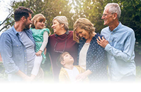 Three generations of a family standing outdoors with trees in background