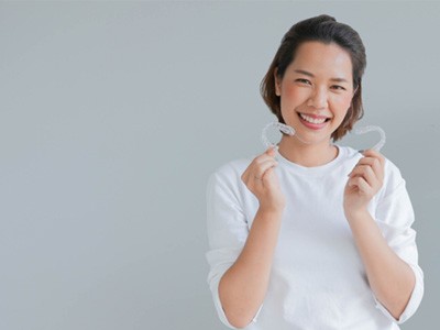 Patient in white shirt holding clear aligners