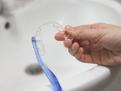 Patient cleaning clear aligner in sink