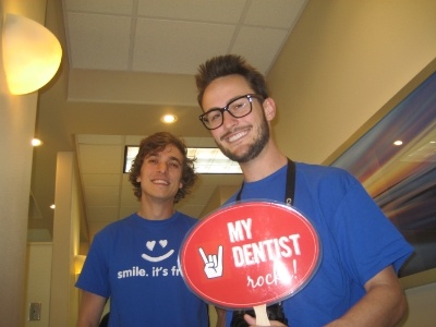 Two young men in dental office with one holding sign that reads my dentist rocks