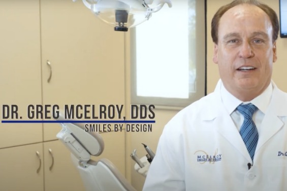 Doctor Greg McElroy in dental exam room with text reading Doctor Greg McElroy D D S Smiles by Design