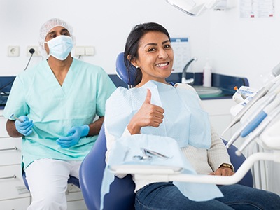 Patient smiling while giving thumbs up in treatment chair