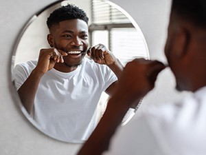 Man smiling at reflection while flossing his teeth