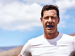 Man in white shirt wearing blue mouthguard outside