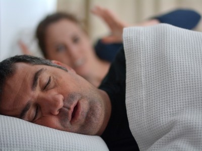 Frustrated woman awake in bed next to snoring man needing sleep apnea treatment