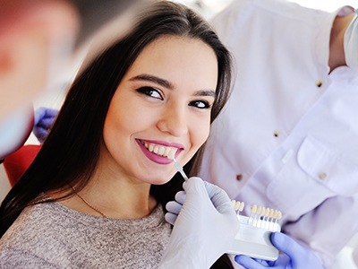 Woman smiling while dentist color-matches veneer