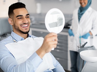 Man smiling at reflection in handheld mirror at dentist's office