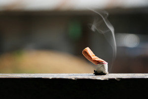 Used cigarette smushed against wooden railing on porch