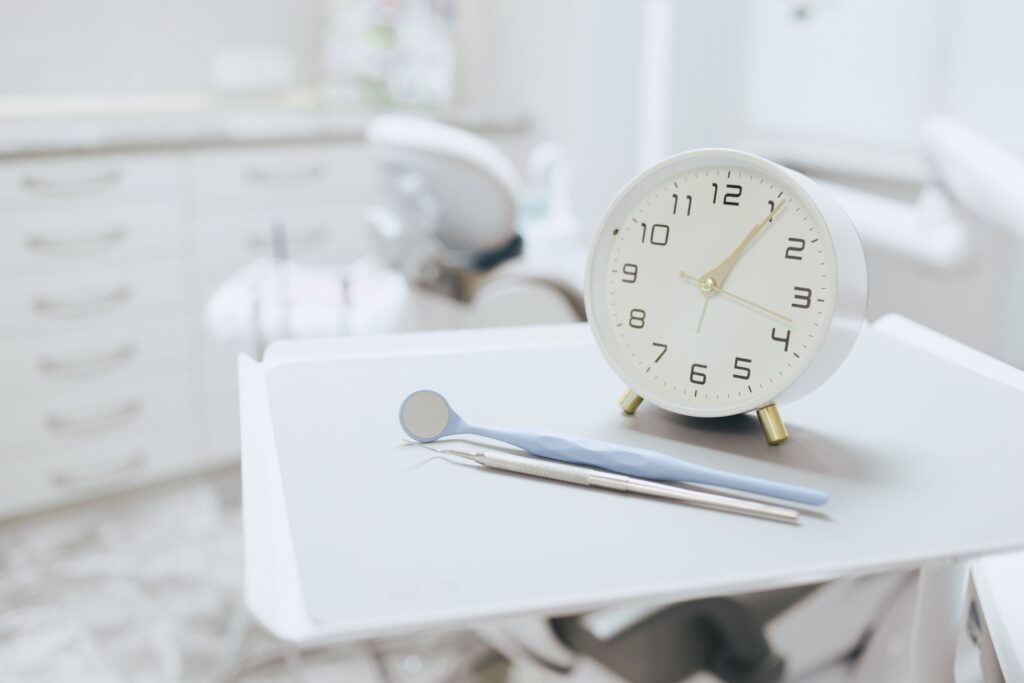 Small white clock on tray next to dental instruments